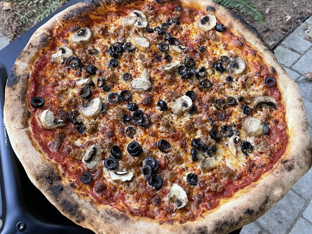 A cooked NY-style pizza with sausage, mushrooms, and olives.