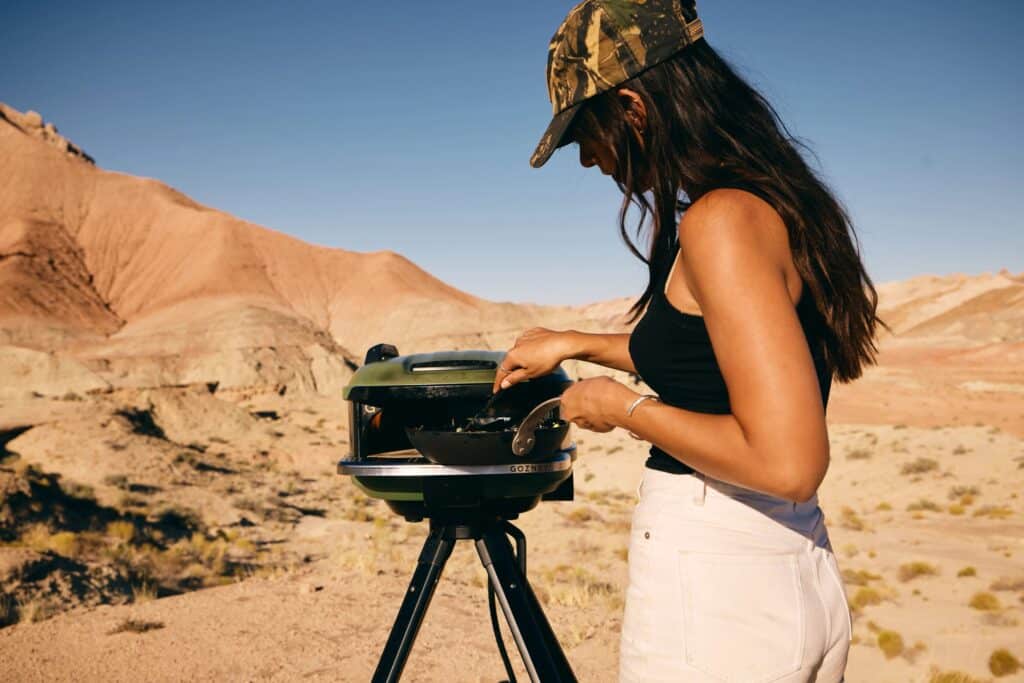 A woman cooking something in a skillet using the Tread in a dessert landscape.
