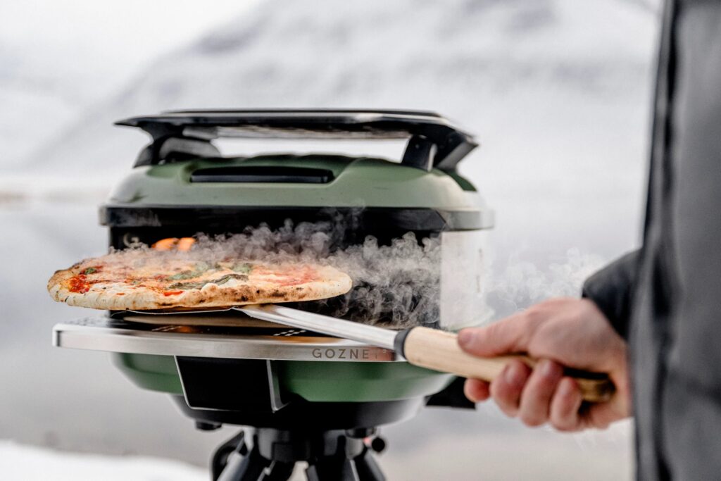 A steaming pizza being pulled out of a Gozney Tread oven with a snowy hill in the background.