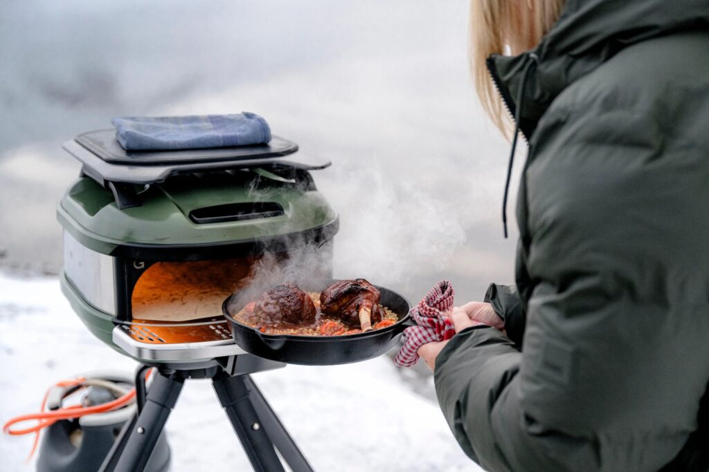 Meat in a skillet being pulled out of a Tread pizza oven with snow in the background.