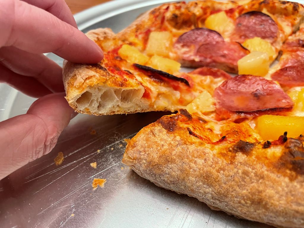 Close up of a New York style pizza with salami and pineapple