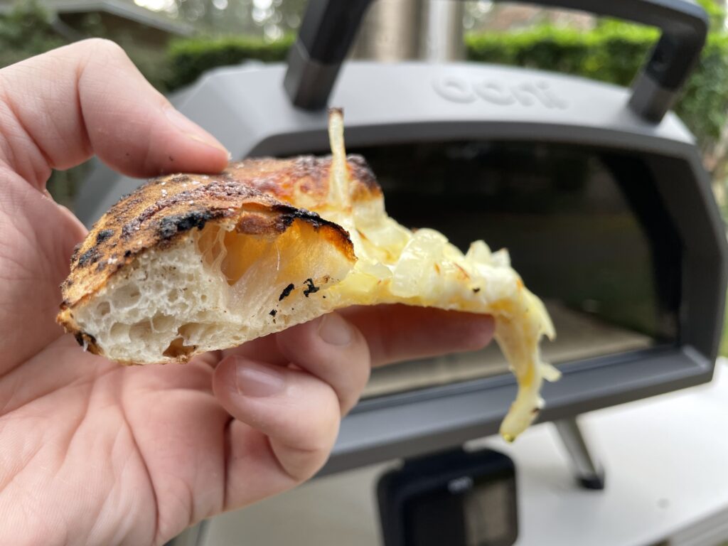 One slice of fugazza held in front of an Ooni pizza oven.