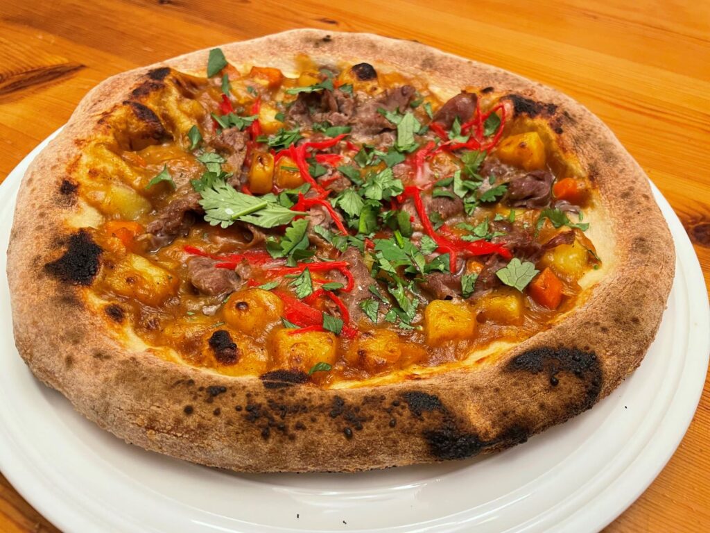 Japanese curry pizza topped with beef, carrots, potato, pickled ginger, and cilantro