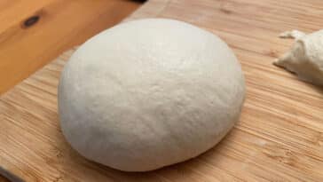 A ball of pizza dough sitting on wood with a kitchen scale in the background.
