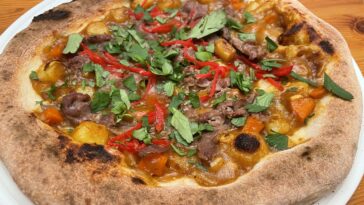 Hero shot of curry pizza with potatoes, carrots, red ginger, and cilantro
