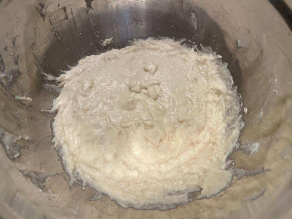 A wet-looking poolish preferment at the bottom of a metal bowl.