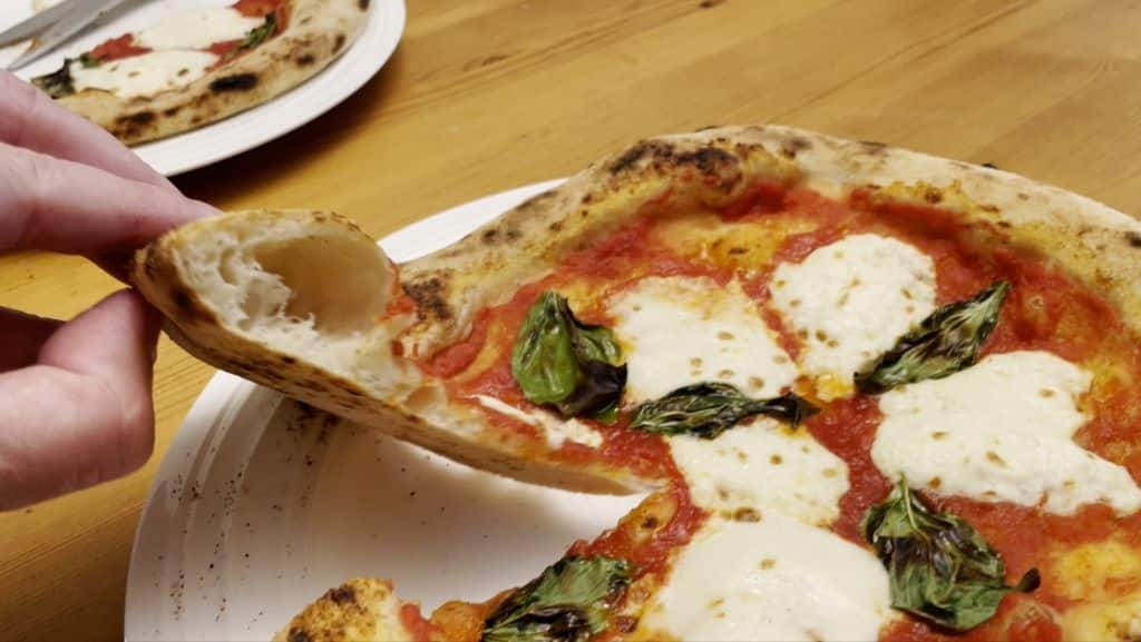 Pizza Party 70x70 Review: An Old-School Wood Burning Monster Pizza Oven Cooked margherita pizza with a slice showing the interior crumb of the crust.