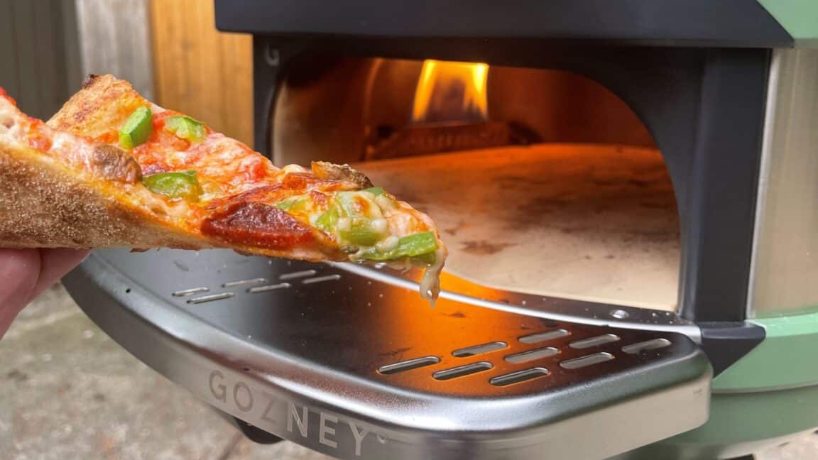 A slice of pizza is displayed in front of the Gozney Tread with the flame running.