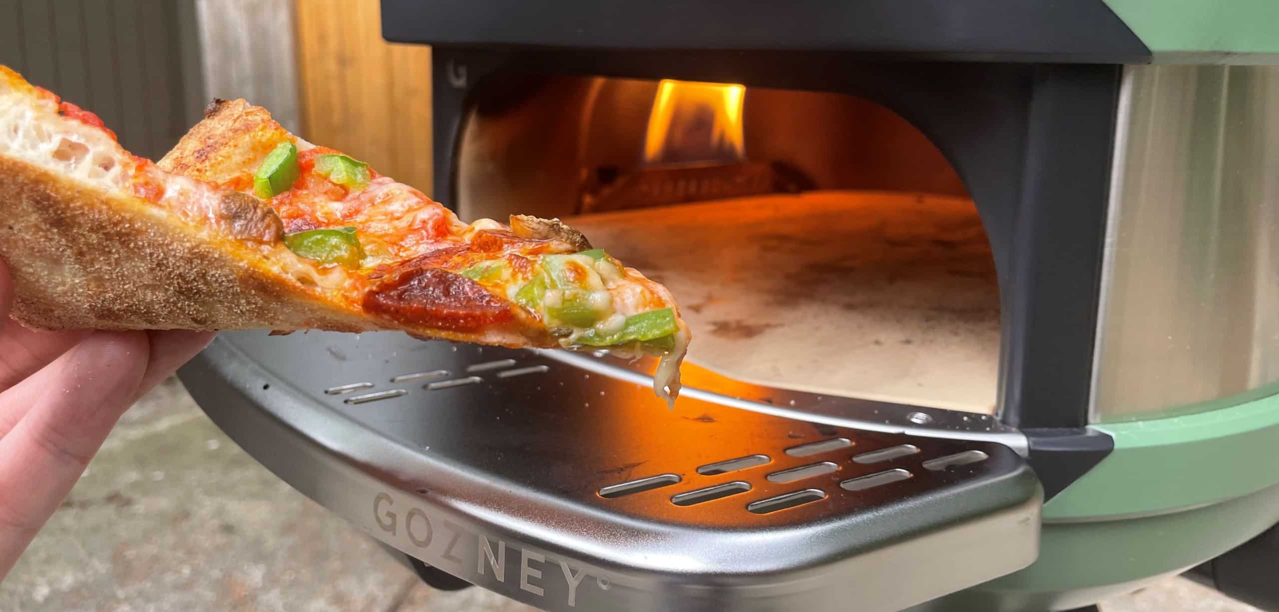 A slice of pizza is displayed in front of the Gozney Tread with the flame running.